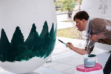 یکی از کودکان نقاش مبتلا به سندرم داون در حال نقاشی بر روی تخم مرغ خود می باشد.