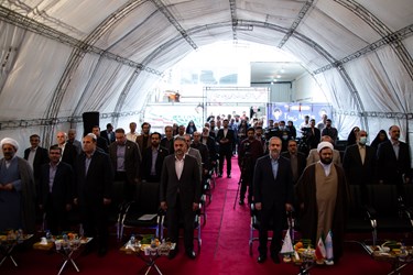 حاضرین درآیین افتتاحیه بازار مشترک کوثر (بامک) به احترام سرود ملی ایران ایستاده اند.