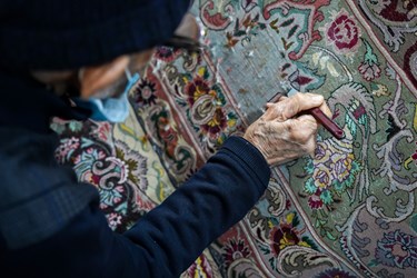 مردی میانسال در حال رفو کردن یک فرش قدیمی است