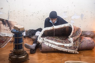 مردی میانسال در حال رفو کردن یک فرش قدیمی است
