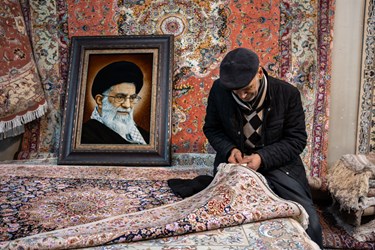 مردی میانسال در حال رفو کردن یک فرش قدیمی است