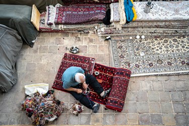 مردی میانسال در حال رفو کردن یک فرش قدیمی است