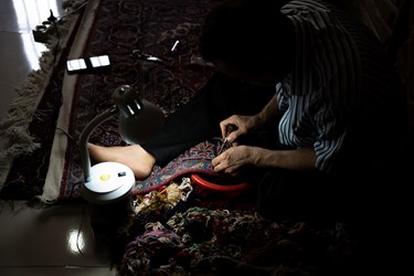 مردی  در حال رفو کردن یک فرش قدیمی است