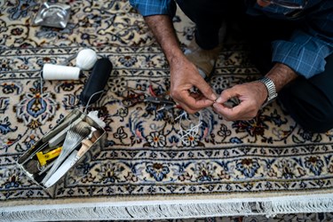 مردی  در حال رفو کردن یک فرش قدیمی است