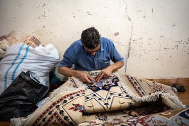مردی  در حال رفو کردن یک فرش قدیمی است