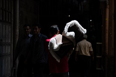 مردی در بازار بزرگ تهران  فرشی را بر دوش خود حمل میکند