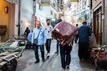مردی در بازار بزرگ تهران  فرشی را بر دوش خود حمل میکند