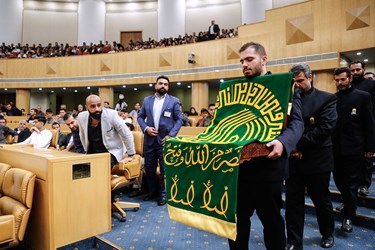 پرچم حرم امام رضا (ع) توسط خادمین به داخل سالن آورده شد.
