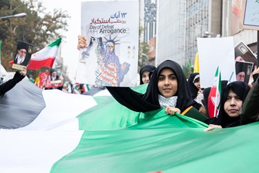 یک دختر پوستری به نشانه مبارزه با استکبار در راهپیمایی 13 آبان در دست دارد