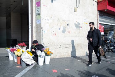 زنی  در حال فروش گل کنار مترو تئاتر شهر تهران است. 10 دی 1402