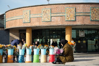 یک خانم بعد از خریدن گل منتظر خانواده اش در محوطه بهشت زهرا تهران است. 28 دی 1402