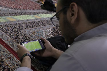 یکی از علاقمندان به فوتبال مشغول تماشای  فوتبال ایران و قطر در مسجد میدان نبوت تهران است