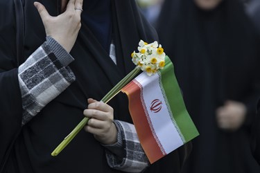 بانویی ایرانی پرچم ایران را همراه با دسته ای گل در جشن 45 سالگی انقلاب در دست گرفته است 