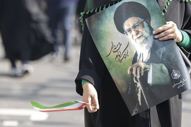 بانویی ایرانی پرچم ایران و پوستر مقام معظم رهبری  را در جشن 45 سالگی انقلاب در دست گرفته است 
